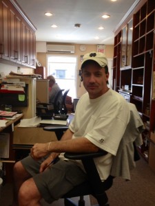 A man sitting in an office chair wearing a white t-shirt and shorts, with a panda-themed hat on his head.