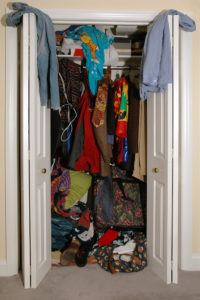 An overstuffed closet with open doors and disorganized contents spilling out.
