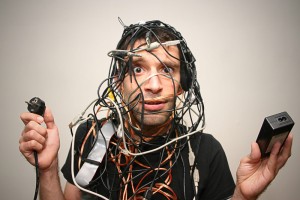A perplexed man entangled in a mess of electrical cords and gadgets.