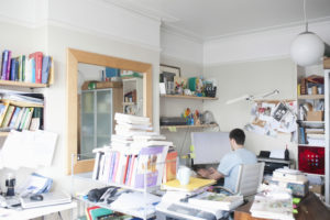 A person working at a computer in a cluttered home office.