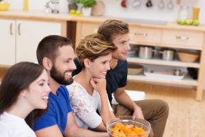 A group of friends enjoying a good time together, possibly watching something off-camera, while sharing snacks in a kitchen setting.