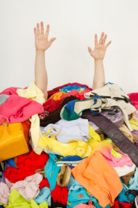 Person buried under a pile of colorful clothes, only hands visible.