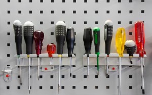 An assortment of kitchen utensils hanging on a metal rack against a pegboard wall.