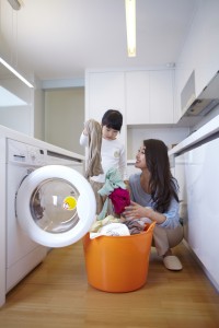 A mother and child are doing laundry together in a brightly lit home interior.
