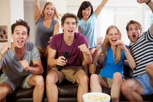 A group of excited friends sitting on a couch, cheering and watching tv.