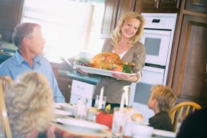 Woman presenting a roasted turkey to family at a dining table.