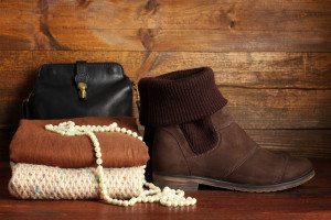 Leather boot, knit scarf, and handbag on wooden background.