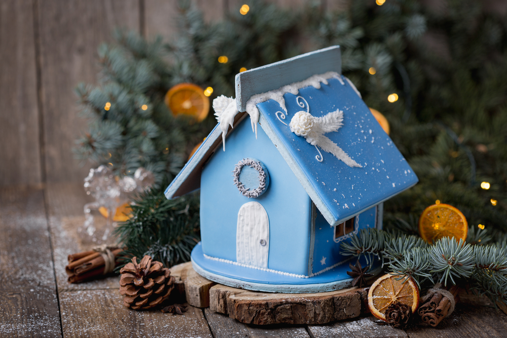 A decorative blue birdhouse with festive holiday adornments, surrounded by pine branches, cones, and sliced dried oranges.