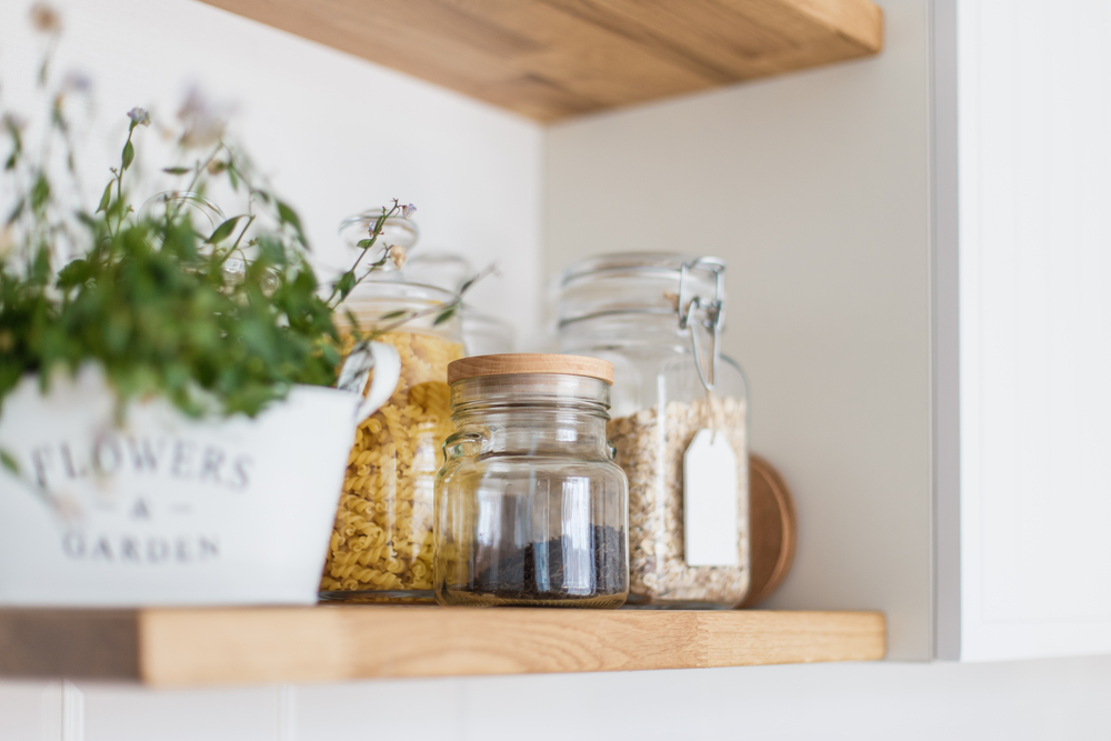 Kitchen shelf with glass jars of dry food and a decorative flowerpot.