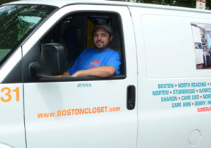 A man in a blue shirt sitting in the driver's seat of a white van with "Boston Closet" branding on the door.