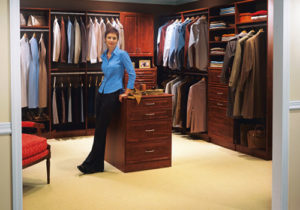 A person standing confidently in one of the well-organized walk-in closets with an array of clothing and a drawer cabinet.