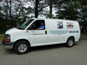 A man sitting in the driver's seat of a white boston closet company van with promotional graphics.