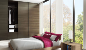 Modern bedroom with large window overlooking greenery, featuring a neatly made bed with red accents and built-in wooden closet.