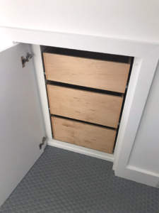 A wooden board obstructing an entryway to an under-stair storage space.