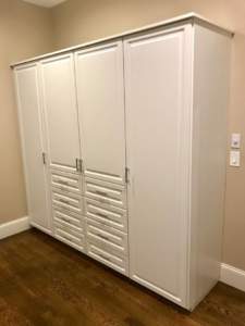 A white built-in closet with closed doors in a room with beige walls and hardwood flooring.