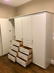 A tall white wardrobe with its drawers pulled out and placed on the floor.