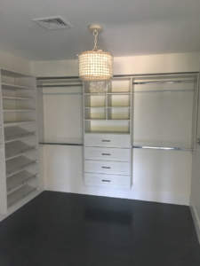 A modern walk-in closet featuring built-in shelves, drawers, and a central island under a chandelier.