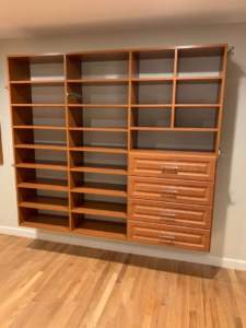 A large wooden shelving unit with empty shelves and drawers against a wall in a room with hardwood flooring.