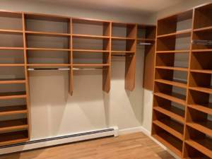 Empty wooden closet organization system installed in a room with beige walls and hardwood flooring.