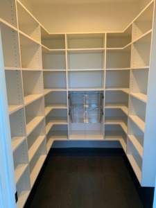 An empty walk-in closet with white shelving and a dark floor.