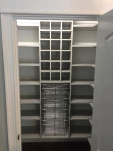 Empty white closet organizer with shelves and a pull-out wire basket.