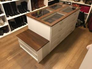 A well-organized closet with a central island featuring drawers and a glass top, surrounded by shelves of shoes.