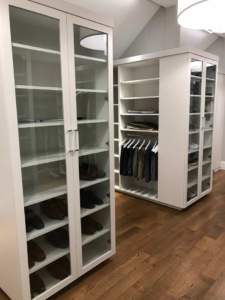 A walk-in closet with white shelving units, displaying shoes and clothing.