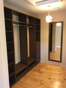A modern, empty wooden wardrobe with drawers and shelves in a room with hardwood flooring and a mirror on the side wall.