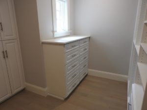 A white chest of drawers placed against a wall in a room with pale walls and wooden flooring.