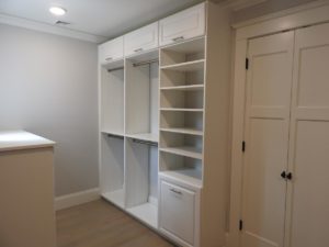 Built-in white closet system featuring shelves, drawers, and a pull-out rack in a room with light walls and flooring.