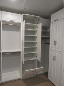 An open white pantry with empty shelves and drawers in a clean, organized room.