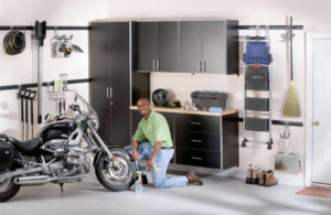 Man kneeling beside a motorcycle in a well-organized garage.
