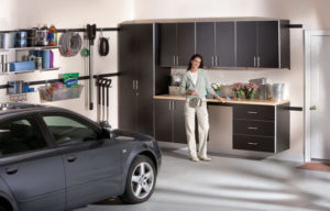 A person standing in a tidy garage with storage cabinets beside a parked car.