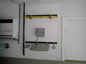 A utility wall with electrical panel, conduits, level tool, and wall-mounted rack in a room.