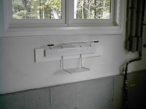Wall-mounted folding white laundry drying rack in a room with a window.