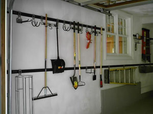 Organized garden tools hanging on a wall-mounted rack in a tidy workshop.