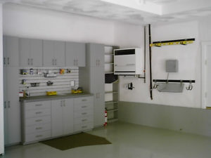 A tidy and organized garage with white storage cabinets, wall-mounted shelves, and a workbench.