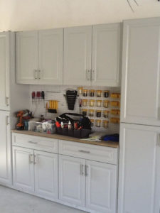 A tidy garage storage area with white cabinets and a pegboard holding various tools and containers.