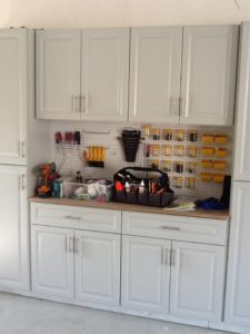 A well-organized garage workspace featuring cabinets, a pegboard with tools, and a workbag on the counter.