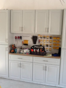 A well-organized garage workspace with white cabinets, a tool pegboard, and storage containers.