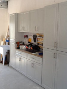 A tidy garage workspace featuring white cabinetry with a pegboard tool organizer and various items on the countertop.