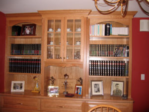 Wooden bookcase with a collection of books, encyclopedias, trophies, and framed photographs.