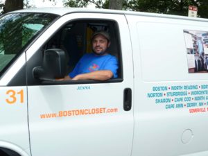 A man in a blue shirt smiling while seated in the driver's seat of a white boston closet company van.