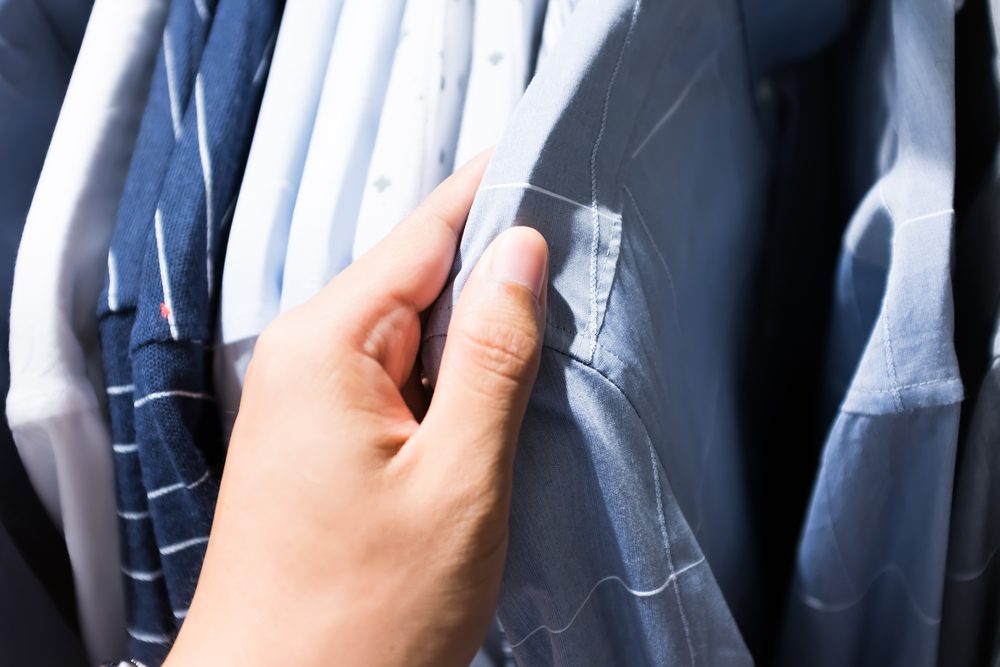 A person's hand browsing through a rack of various blue and white shirts.