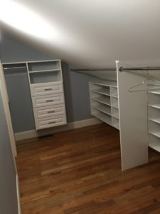 An empty walk-in closet with white shelving and hanging space under a sloped ceiling.