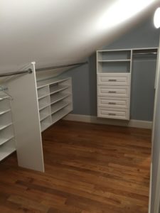 A clean, empty walk-in closet featuring built-in shelves and drawers with hardwood flooring.