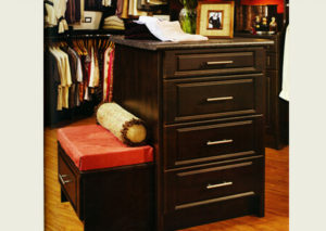 Wooden dresser with drawers in a walk-in closet, accompanied by a bench with a red cushion.