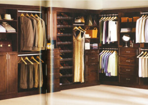An elegantly organized walk-in closet with wooden cabinetry and a variety of clothing items on display.