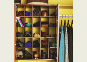 A variety of shoes, bags, and umbrellas organized on a shelving unit next to hanging clothing.