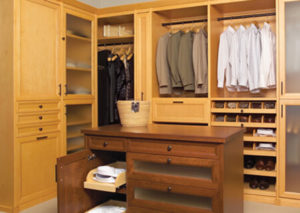 A neatly organized walk-in closet with wooden cabinets and clothing.
